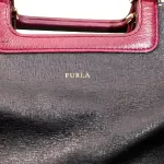 Furla tri-colour two-way handbag in black, white and maroon, close-up of maroon handles and Furla logo