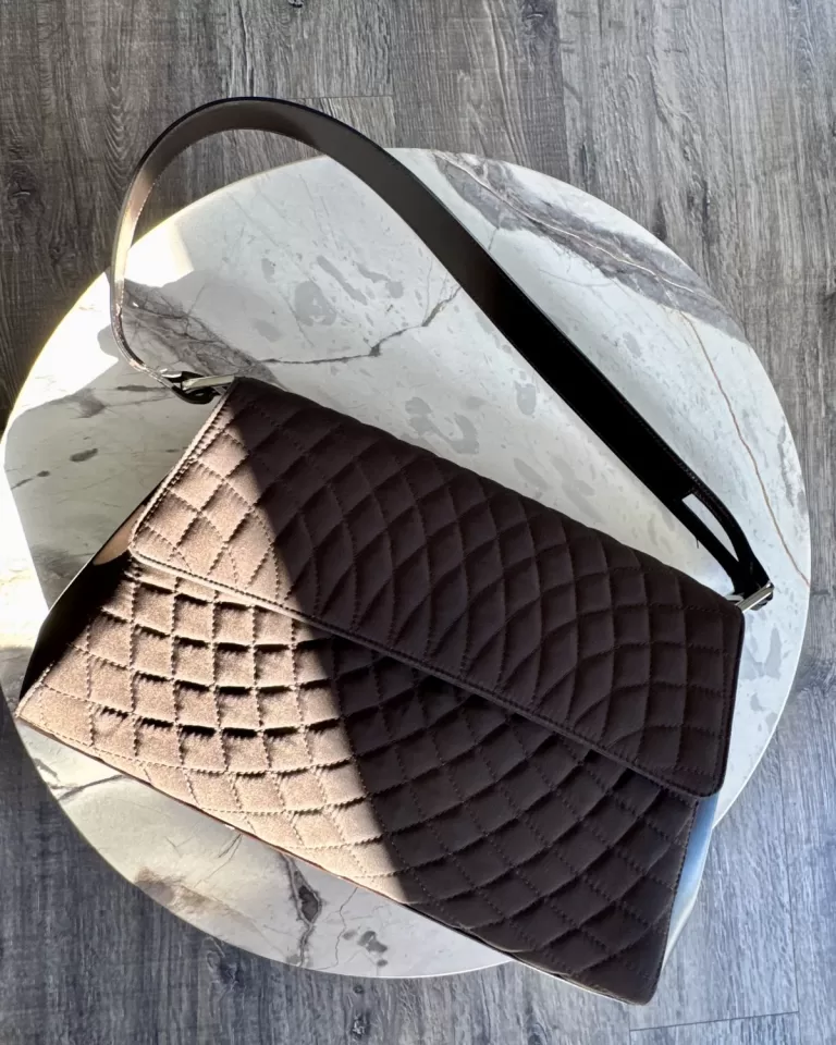 Quilted leather clutch bag styled on marble and wood, editorial still life