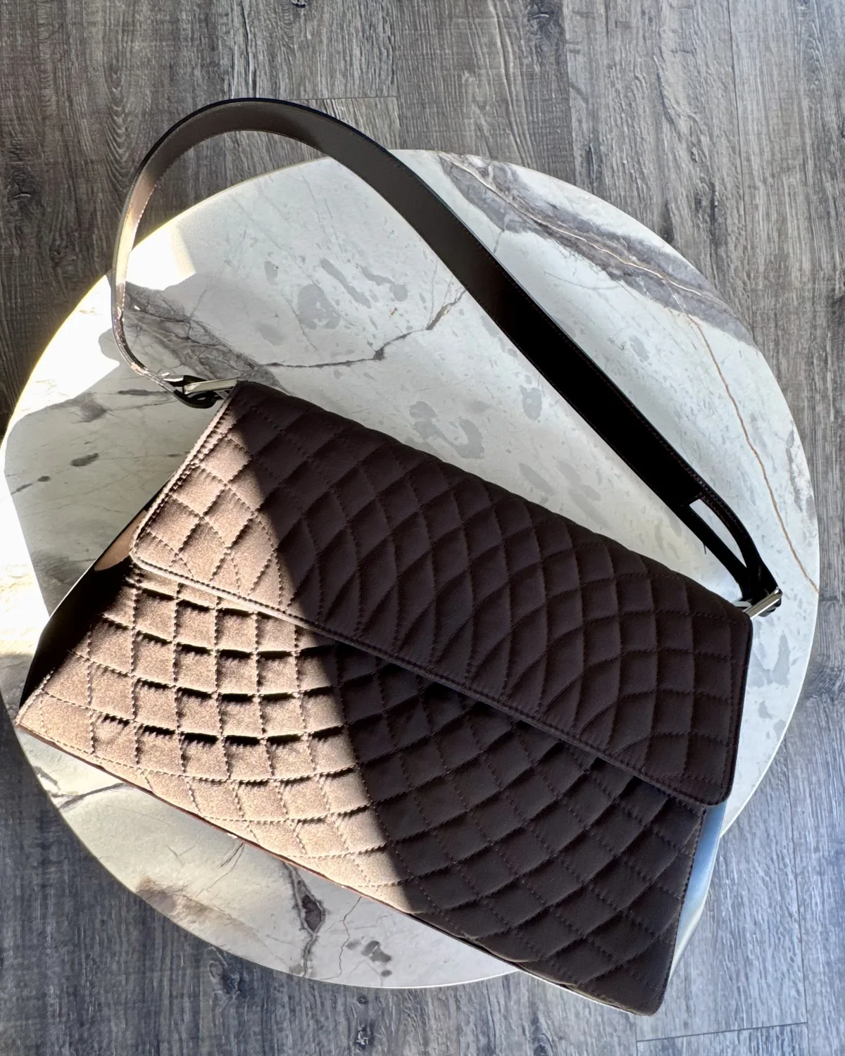 Quilted leather clutch bag styled on marble and wood, editorial still life