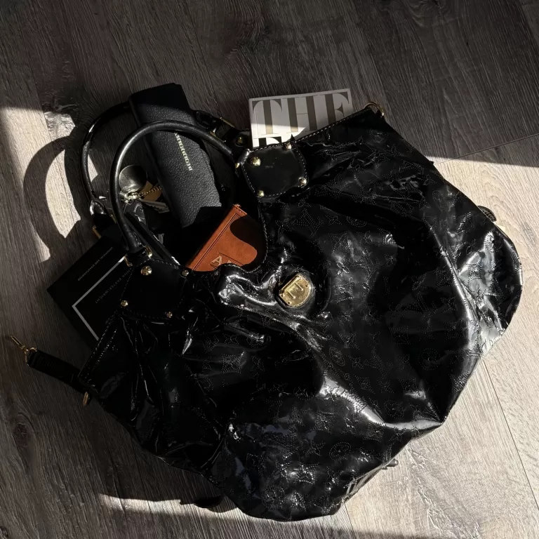 Black patent Louis Vuitton bag with gold hardware on a wooden floor, styled with a card holder and sunglasses case